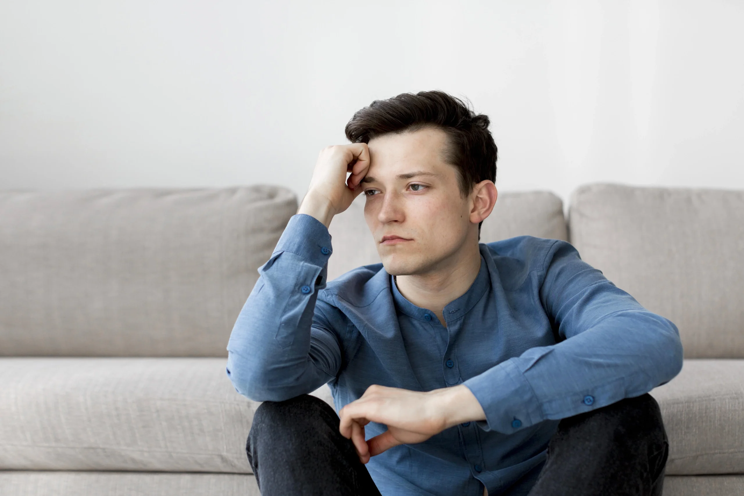 Young man sitting on a sofa looking stressed and anxious, reflecting the importance of addressing men's mental health during Men's Mental Health Month.