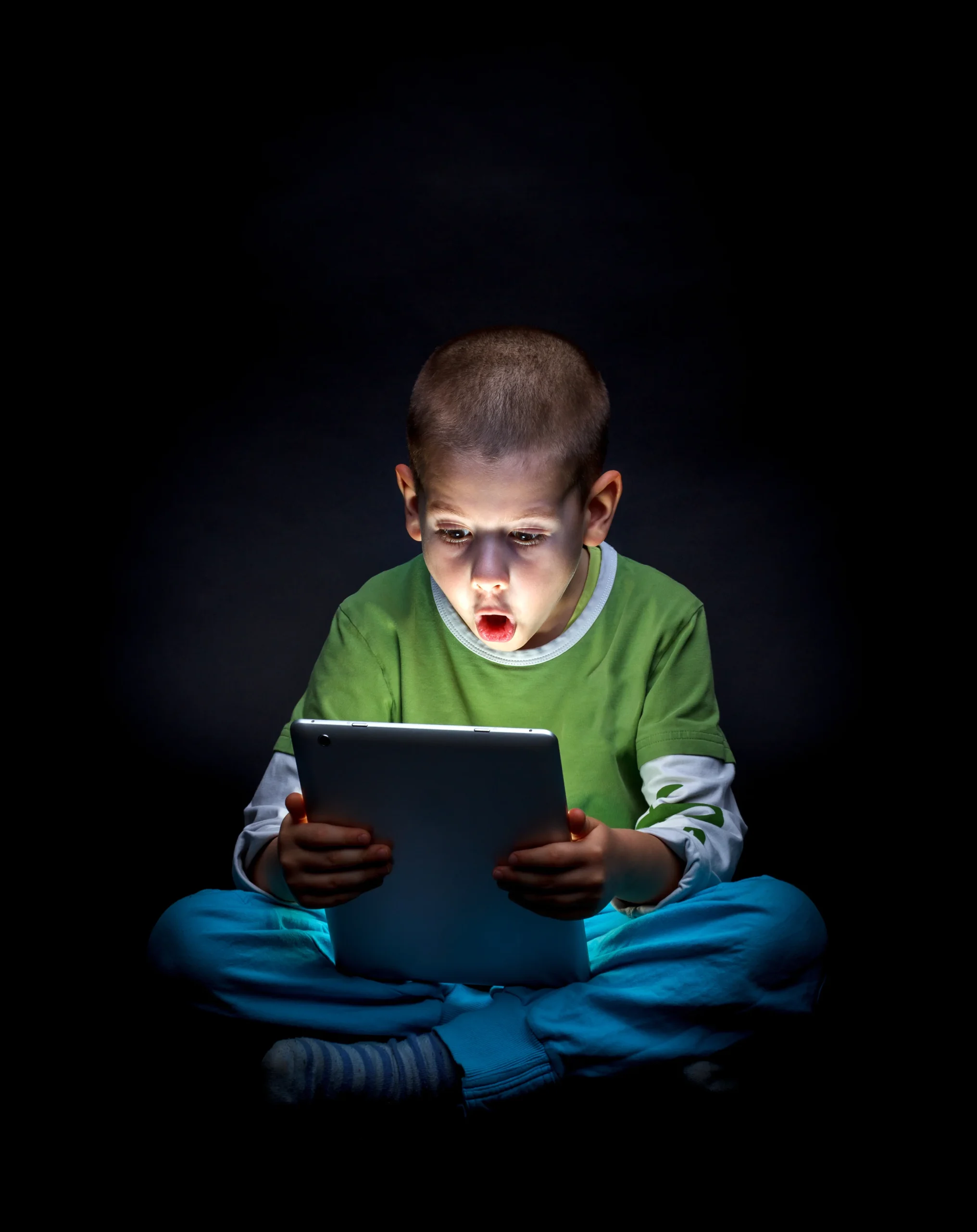 A child staring at a tablet screen in the dark, illustrating Screen time Effects On Children, with a look of surprise or focus.