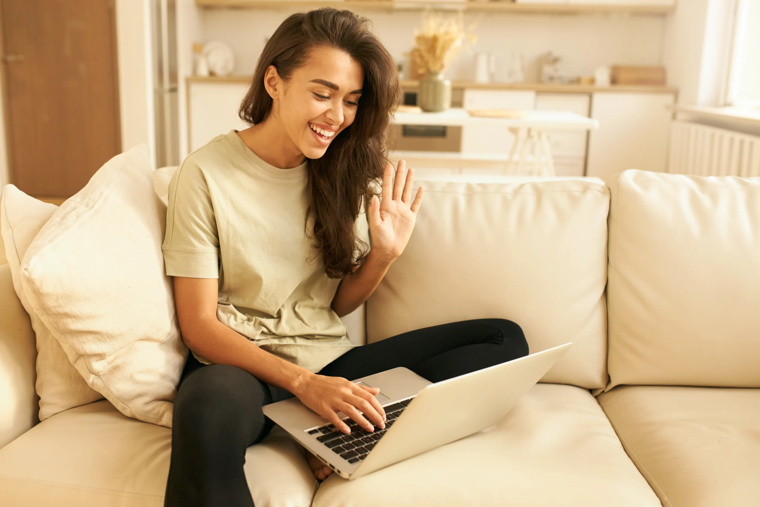 A woman smiling and waving while video chatting on her laptop, showcasing the importance of virtual connections for social well-being and mental health, supported by digital mental health apps.
