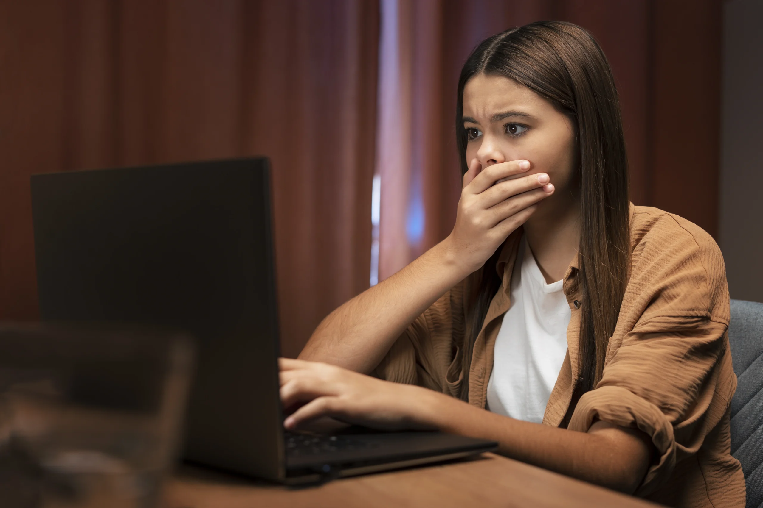 Teen girl looking shocked at laptop screen, highlighting social media and mental health challenges linked to cyberbullying.