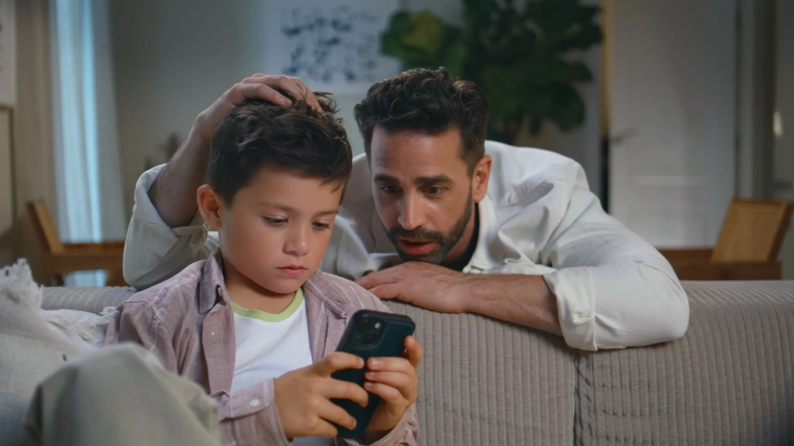 Father engaging with his son while he plays on his smartphone, highlighting the importance of monitoring kids' mental health in a digital world.