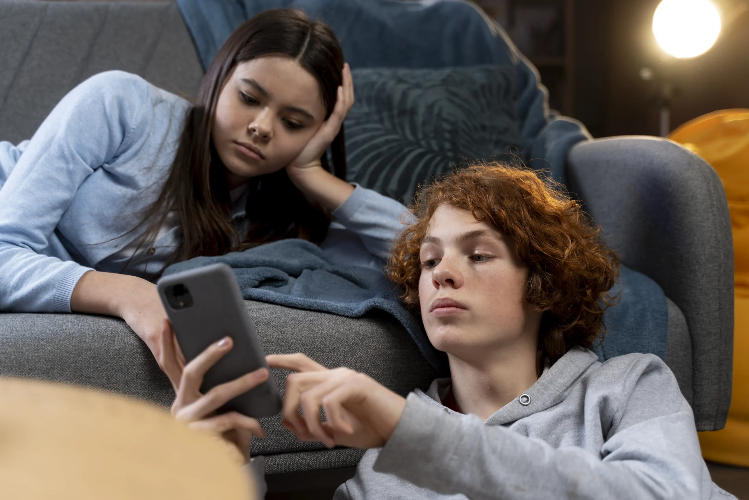 Cyberbullying and mental health concerns as two teenagers look at a smartphone together at home.