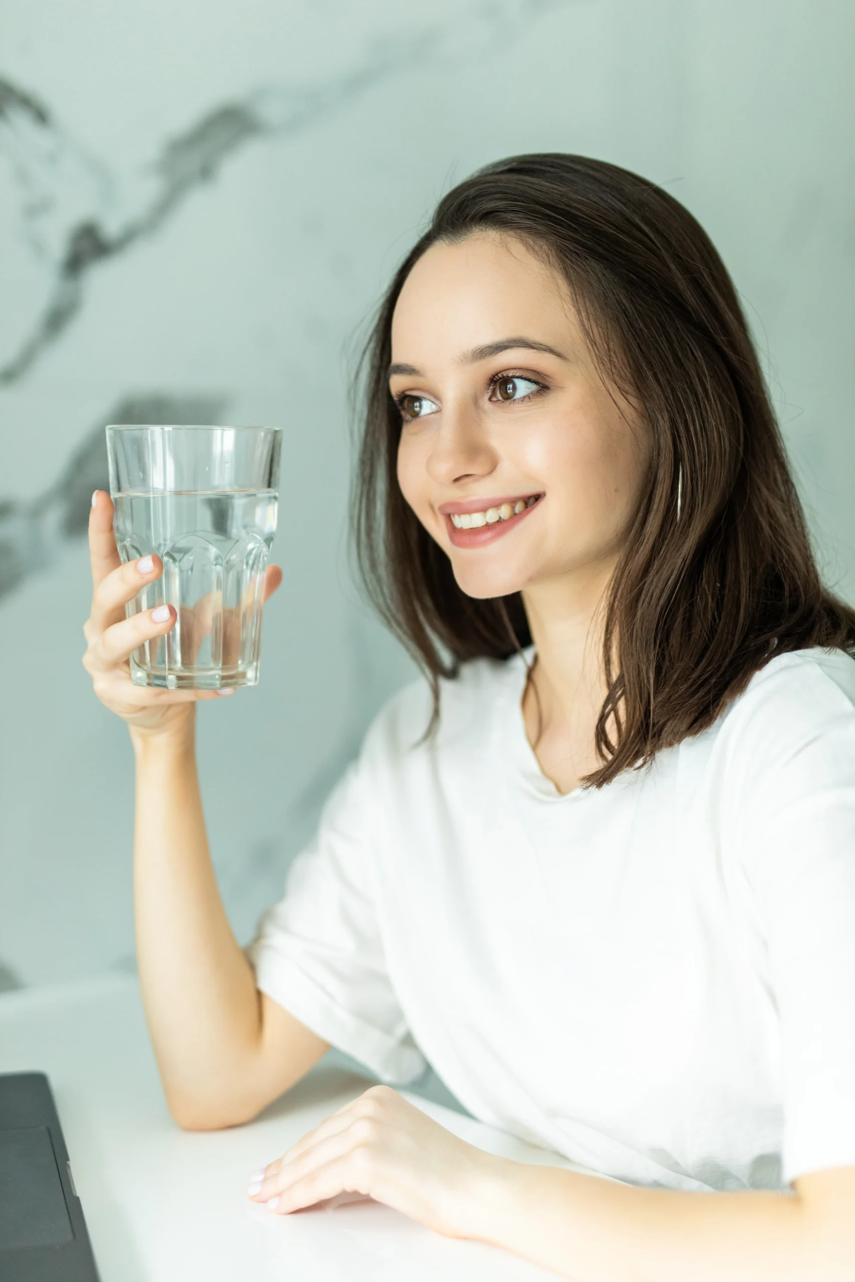 How to get hydrated fast: A young woman holding a glass of water, smiling and enjoying a refreshing drink to quickly hydrate her body."