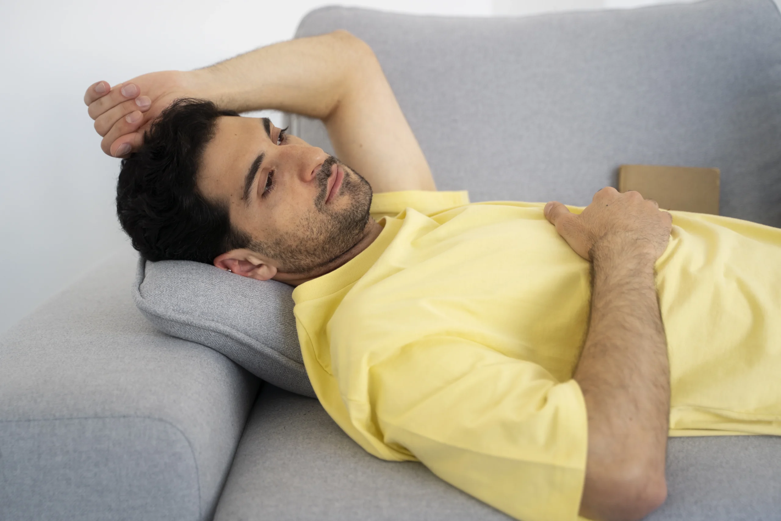 A man resting on the couch, showing one of the early signs your body needs rest, as he relaxes and takes a break from daily stress and fatigue.
